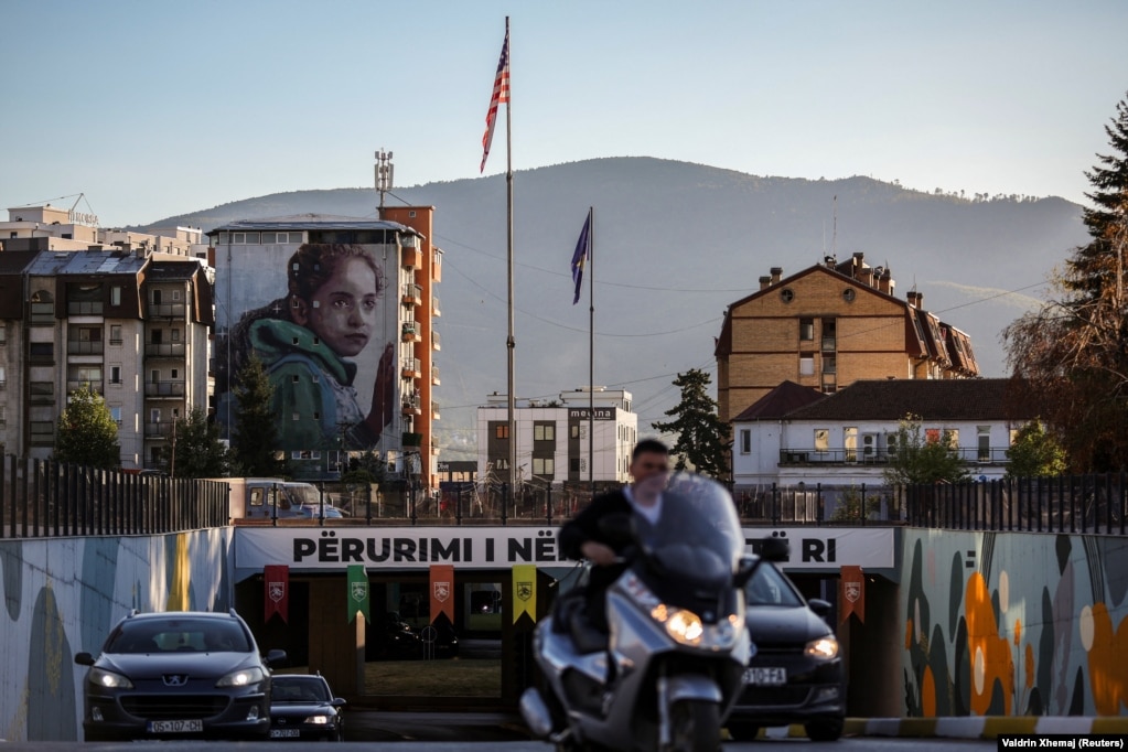 Një nga mbi 200 muralet e Ferizajt shihet në prapavijë teksa automjetet qarkullojnë në qytet.
