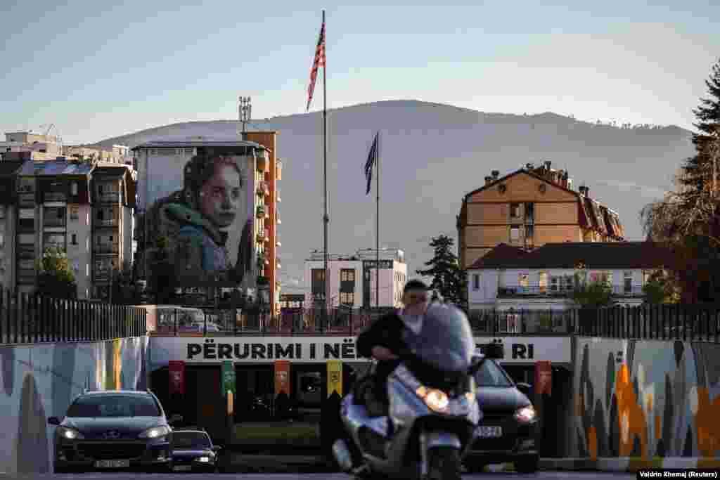 Një nga mbi 200 muralet e Ferizajt shihet në prapavijë teksa automjetet qarkullojnë në qytet.