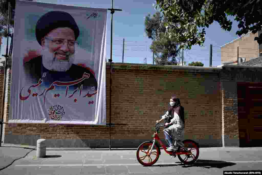 Иранская девушка проезжает на велосипеде мимо огромного плаката с изображением консервативного кандидата в президенты Ирана Эбрахима Раиси в Тегеране