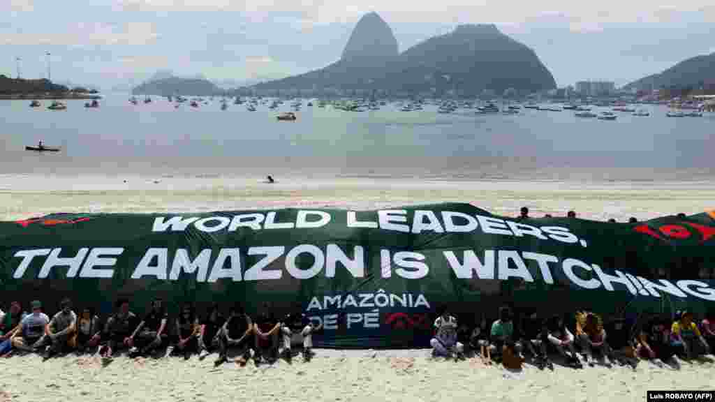 Környezetvédő aktivisták a Botafogo strandon egy óriási transzparenst mutatnak, amelyen ez áll: Világ vezetői, az Amazonas figyel. A háttérben a Cukorsüveg-hegy Rio de Janeiróban 2024. november 17-én, a G20-ak csúcstalálkozója előtt.&nbsp;A G20-országok a világgazdaság 85 százalékát adják, és az üvegházhatású gázok kibocsátásának több mint háromnegyedéért is ők a felelősek