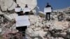 Muškarci stoje usred ruševina uništenih kuća sa plakatima na kojima kritiziraju Ujedinjene nacije, u Atarebu, Sirija, 12. februara 2023.