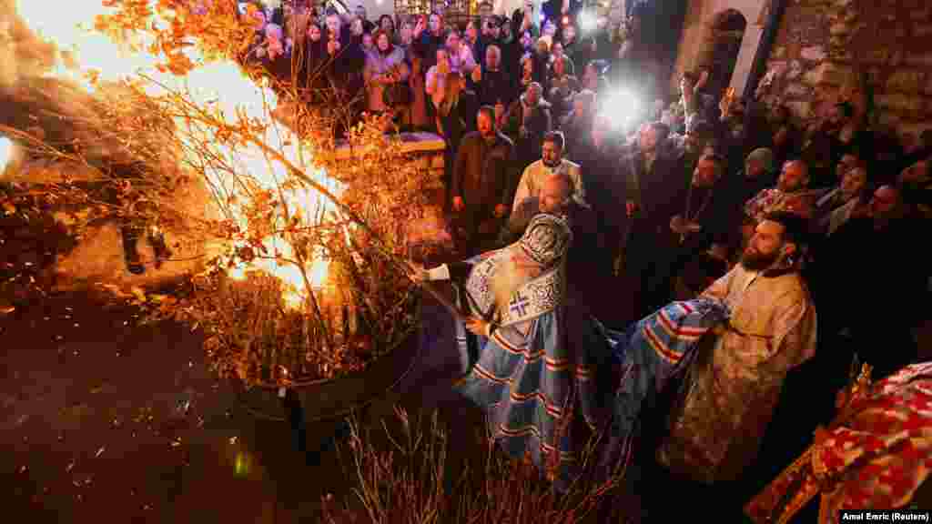 Hrizostom Jević, bosanski prelat Srpske pravoslavne crkve, stavlja osušena hrastova drva na vatru ispred crkve u Sarajevu 6. januara u sklopu balkanske tradicije spaljivanja hrastovih grana, koje simboliziraju badnjak, na pravoslavni Badnjak.