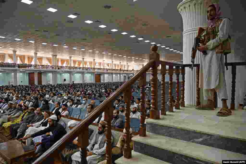 Борец во сандали стои стража додека високиот талибански лик Абдул Хакани се обраќа на состанокот за мажи за образовните политики на Талибанците во салата Лоја Јирга во Кабул на 29 август.