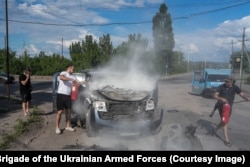 Local volunteer Bohdan Zuyakov (left) helps to extinguish the car after the drone strike.