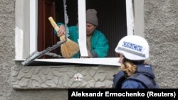 A member of the OSCE walks past a local resident, who removes debris inside a house damaged during recent fighting between Ukrainian forces and Russia-backed separatists in Luhansk in eastern Ukrainie. 