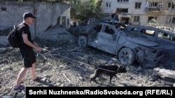 Мужчина выгуливает собаку на месте попадания в жилой дом во время ночной атаки на Киев, 20 августа 2026 года