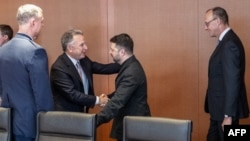 Președintele ucrainean, Volodimir Zelenski, salutându-l pe emisarul american, Steve Witkoff, înainte de convorbiri găzduite la Berlin de cancelarul german, Friedrich Merz (dreapta) pe 14 decembrie 2025