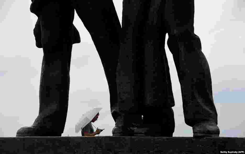 A man stands under an umbrella beneath a Soviet-era monument as rain falls in the Ukrainian capital, Kyiv. (AFP/Sergei Supinsky)