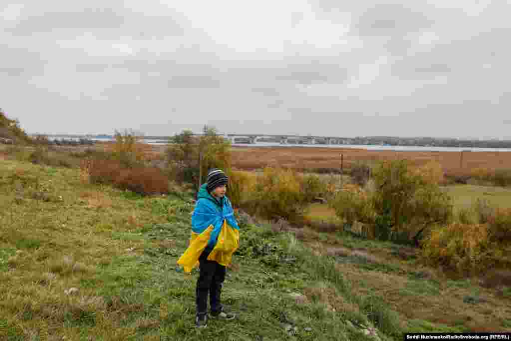 Загорнутий в прапор України хлопчик стоїть на березі Дніпра, неподалік від Антонівського мосту. Фото від листопада 2022 року.Тоді ж, у листопаді, від російської окупації було звільнене місто Херсон