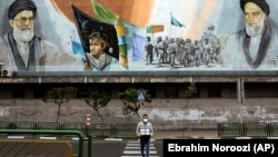 A man crosses an empty street under portraits of the late Iranian revolutionary founder Ayatollah Khomeini, right, and Supreme Leader Ayatollah Ali Khamenei, left, in Tehran, April 3, 2020