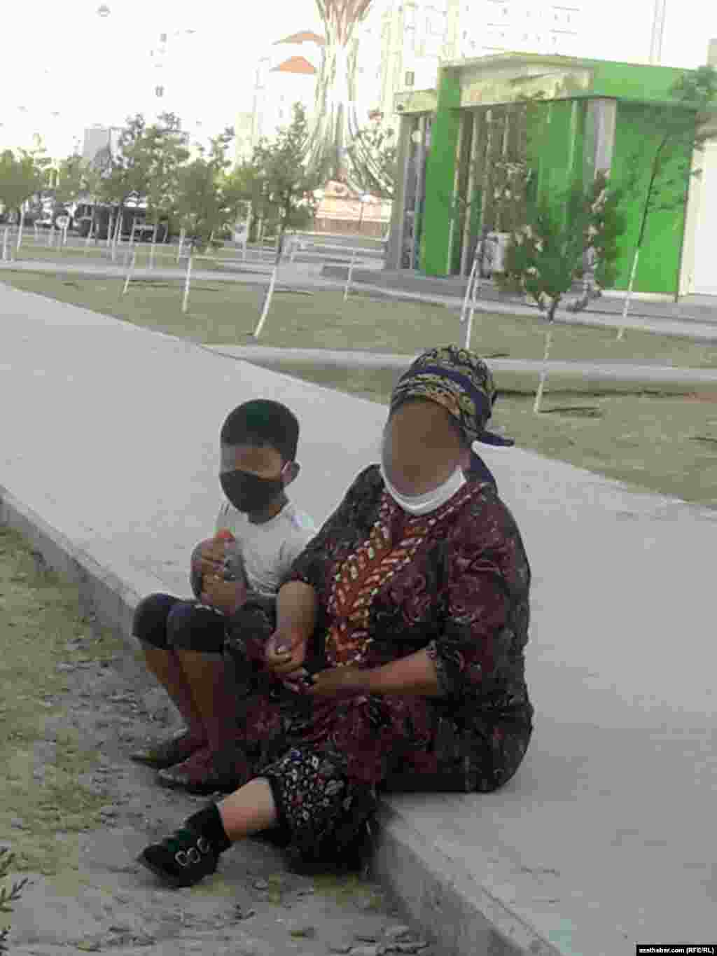Aşgabat. Ýanýolda oturyp, ogly bilen dynç alýan aýal. Awgust, 2020.