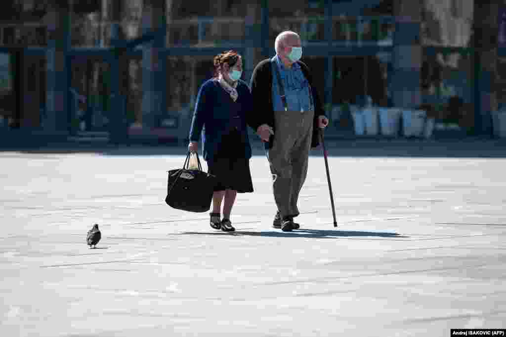 An elderly couple wearing protective masks take a walk in Belgrade&#39;s main square on March 17. (AFP/Andrej Isakovic)