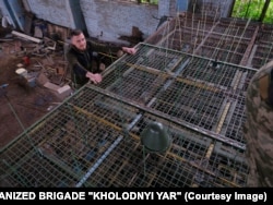 A Ukrainian crew fits plastic wires to a cage designed to fit over a tank