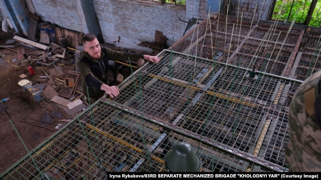 Ukraynalı hərbçilər dron pərlərini ilişdirmək üçün metal qəfəsə plastik məftillər quraşdırırlar.