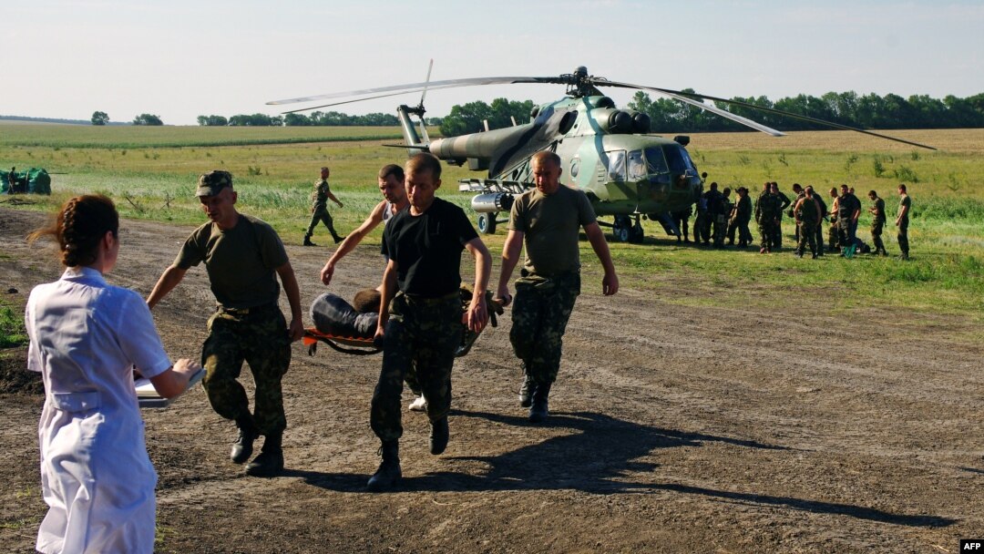Ukrainian soldiers carry a wounded comrade on a stretcher, with a Ukrainian helicopter and other troops in the background, on July 31 in a field near Zaporizhya.
