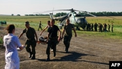 Ukrainian soldiers carry a wounded comrade on a stretcher, with a Ukrainian helicopter and other troops in the background, on July 31 in a field near Zaporizhya.